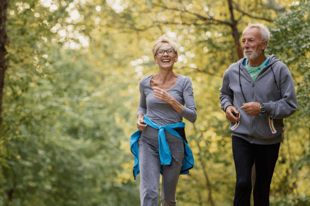 Married couple, age 60, is jogging along a wooded pathway.